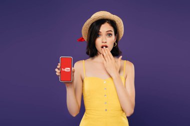 Kiev, Ukrayna - 3 Temmuz 2019: hasır şapkalı kız fikir jesti gösteren ve mor izole youtube logosu ile akıllı telefon tutarak