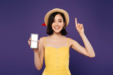 Kiev, Ukrayna - 3 Temmuz 2019: hasır şapkalı heyecanlı kız fikir jesti gösteriyor ve mor üzerinde izole gmail uygulaması ile akıllı telefon tutuyor