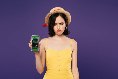 mor izole rezervasyon uygulaması ile akıllı telefon tutan hasır şapka üzgün güzel kız 