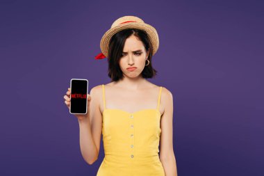 Kiev, Ukrayna - 3 Temmuz 2019: mor izole netflix uygulaması ile akıllı telefon tutan hasır şapka üzgün güzel kız 