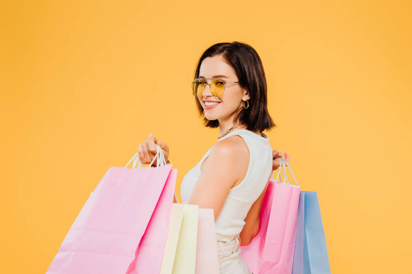 smiling happy woman in sunglasses holding shopping bags isolated on yellow