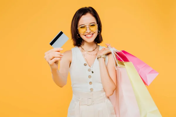 Happy Girl Sunglasses Shopping Bags Presenting Credit Card Isolated Yellow — Stock Photo, Image