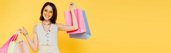 黄色で隔離されたショッピングバッグを保持するサングラスで幸せなファッショナブルな女の子のパノラマショット — ストック写真