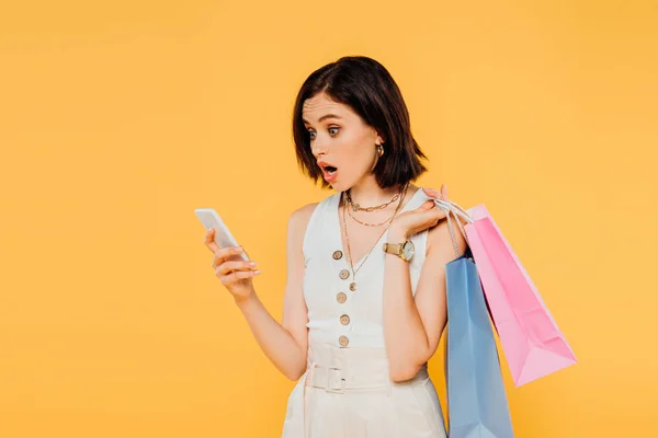 Chocado Chica Con Bolsas Compras Hablando Teléfono Inteligente Aislado Amarillo — Foto de Stock