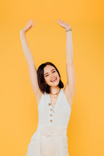 smiling elegant girl with hands in air isolated on yellow