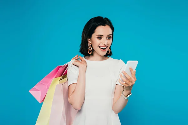 Szczęśliwa Elegancka Kobieta Sukni Torby Zakupy Trzymając Smartphone Izolowane Niebiesko — Zdjęcie stockowe