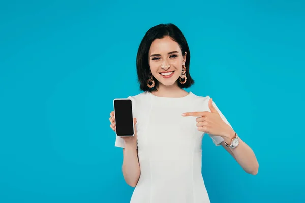 微笑优雅的女人在礼服指着手指在智能手机与空白屏幕隔离在蓝色 — 图库照片