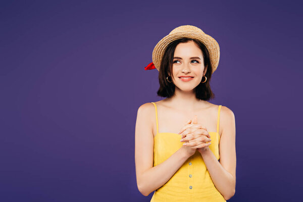 smiling girl in straw hat with clenched hands looking away isolated on purple