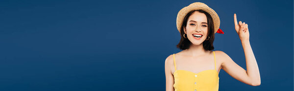 panoramic shot of smiling girl in straw hat showing idea gesture isolated on blue