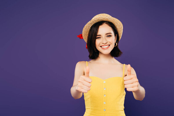 smiling pretty girl in straw hat showing thumbs up isolated on purple