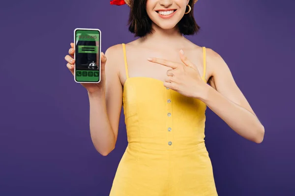 紫色に隔離された予約アプリでスマートフォンで指を指して指を指すわら帽子の女の子のトリミングビュー — ストック写真