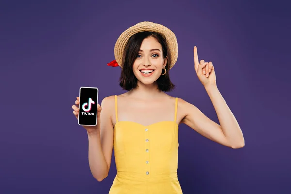 乌克兰 2019年7月3日 兴奋的女孩在草帽显示想法手势和拿着智能手机与Tiktok应用程序隔离在紫色 — 图库照片