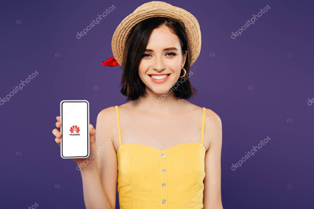 KYIV, UKRAINE - JULY 3, 2019: smiling girl in straw hat holding smartphone with huawe logo isolated on purple