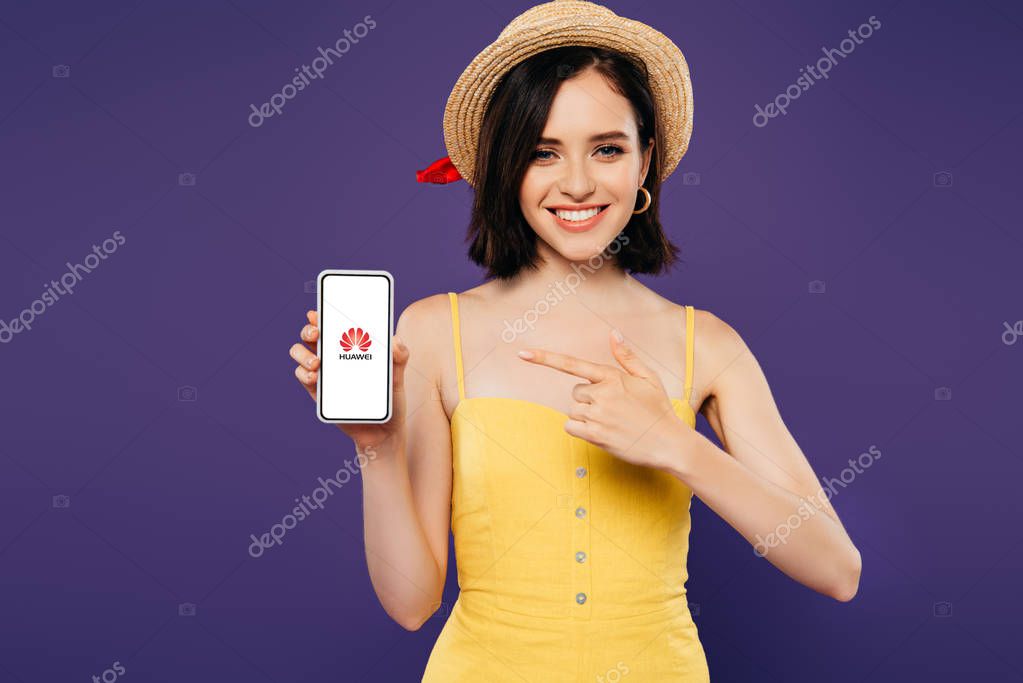 KYIV, UKRAINE - JULY 3, 2019: smiling girl in straw hat pointing with finger at smartphone with huawei logo isolated on purple
