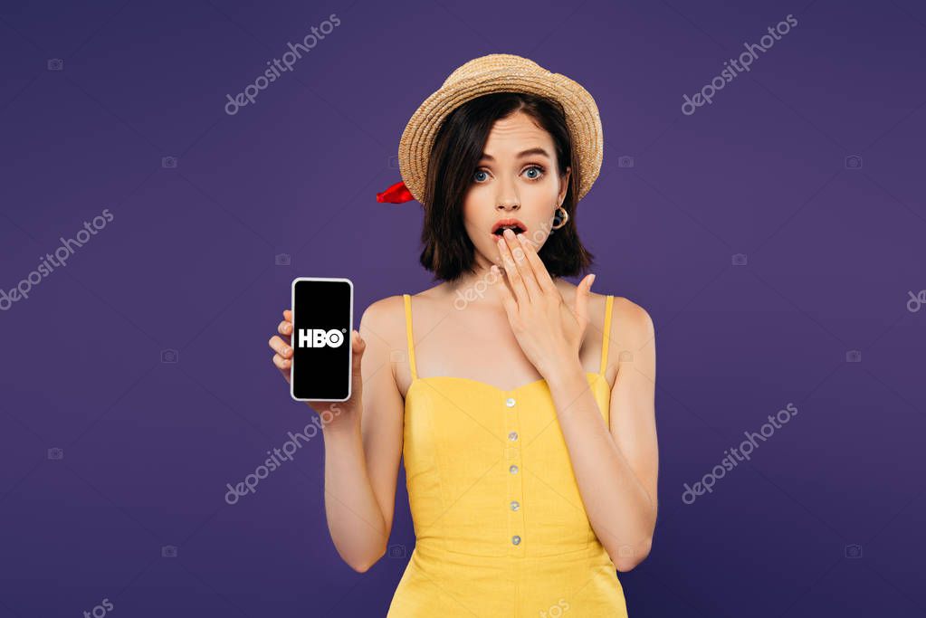 KYIV, UKRAINE - JULY 3, 2019: girl in straw hat showing idea gesture and holding smartphone with HBO logo isolated on purple