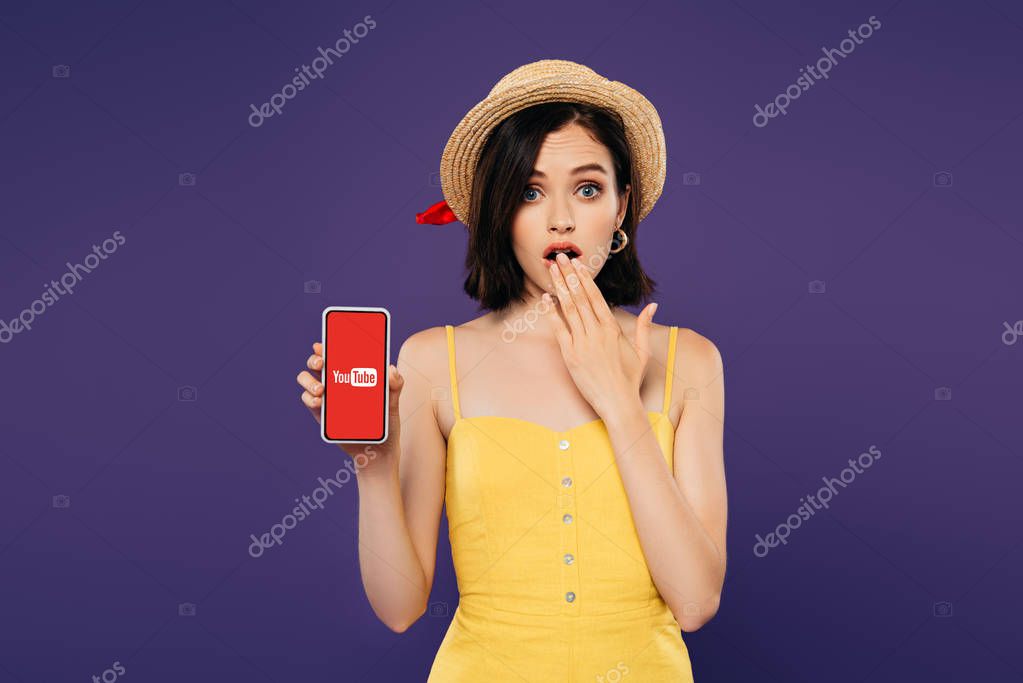 KYIV, UKRAINE - JULY 3, 2019: girl in straw hat showing idea gesture and holding smartphone with youtube logo isolated on purple