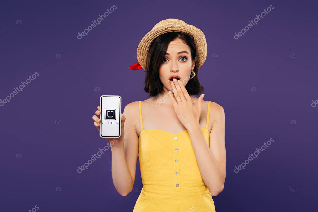 KYIV, UKRAINE - JULY 3, 2019: girl in straw hat showing idea gesture and holding smartphone with uber logo isolated on purple