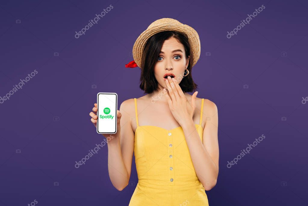 KYIV, UKRAINE - JULY 3, 2019: girl in straw hat showing idea gesture and holding smartphone with Spotify logo isolated on purple
