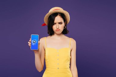 Kiev, Ukrayna - 3 Temmuz 2019: shazam uygulaması mor izole ile akıllı telefon tutan hasır şapka üzgün güzel kız 