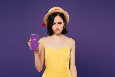 Kiev, Ukrayna - 3 Temmuz 2019: mor izole instagram uygulaması ile akıllı telefon tutan hasır şapka üzgün güzel kız 
