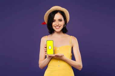 Kiev, Ukrayna - 3 Temmuz 2019: mor izole snapchat uygulaması ile akıllı telefon tutan hasır şapka güzel kız gülümseyen 