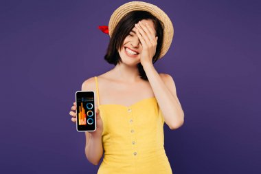 mor izole iş uygulaması ile akıllı telefon gösteren yüzünde el ile hasır şapka gülümseyen güzel kız 