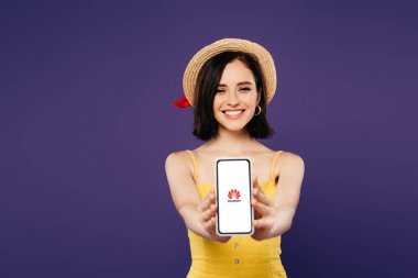 Kiev, Ukrayna - 3 Temmuz 2019: mor izole huawei logosu ile akıllı telefon sunan hasır şapka gülümseyen güzel kız seçici odak 