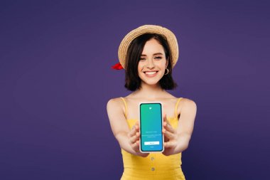 Kiev, Ukrayna - 3 Temmuz 2019: mor izole twitter uygulaması ile akıllı telefon sunan hasır şapka güzel kız gülümseyen seçici odak 