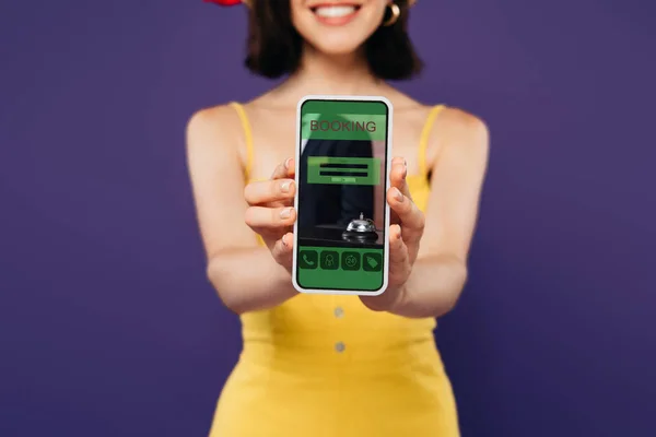 Селективный Фокус Улыбающейся Девушки Представляющей Смартфон Приложением Бронирования Изолированным Фиолетовый — стоковое фото
