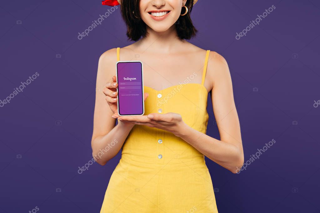 KYIV, UKRAINE - JULY 3, 2019: cropped view of smiling girl holding smartphone with instagram app isolated on purple