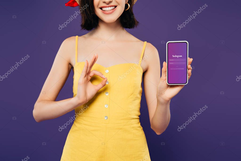 KYIV, UKRAINE - JULY 3, 2019: cropped view of smiling girl in holding smartphone with Instagram app and showing ok sign isolated on purple