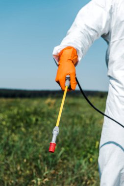 cropped view of exterminator in orange latex glove and white uniform holding spray outside  clipart