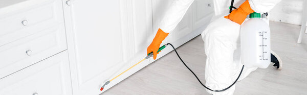 панорамный снимок дезинсектора в защитной маске с помощью токсичного спрея возле кухонного шкафа
 