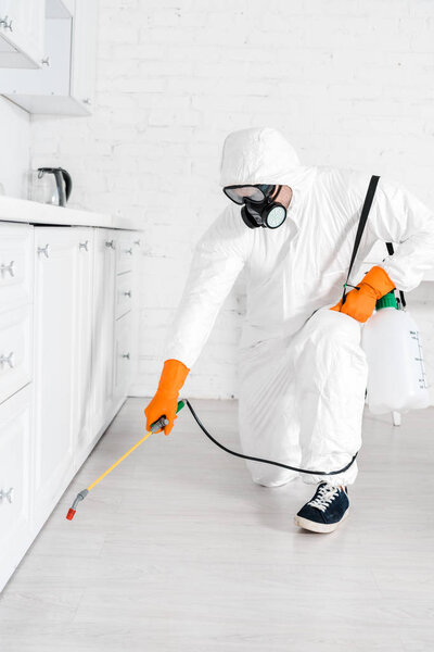 дезинсектор в защитной маске с помощью токсичного спрея возле кухонного шкафа
 