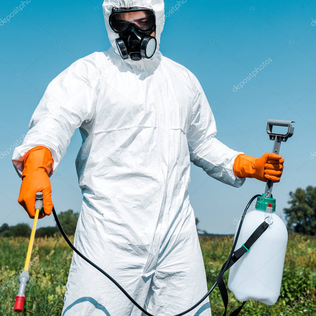 exterminator in orange latex gloves and white uniform holding spray outside 