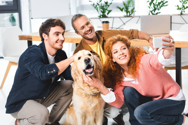 three smiling friends taking selfie with cute golden retriever