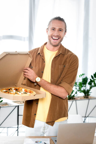 handsome and smiling businessman holding box with pizza in office 