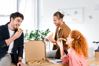 üç gülümseyen arkadaşlar pizza yemek ve ofiste evrak yapıyor 