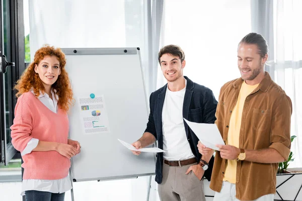 Drie Glimlachende Vrienden Houden Papers Buurt Van Flipchart Kijken Naar — Stockfoto