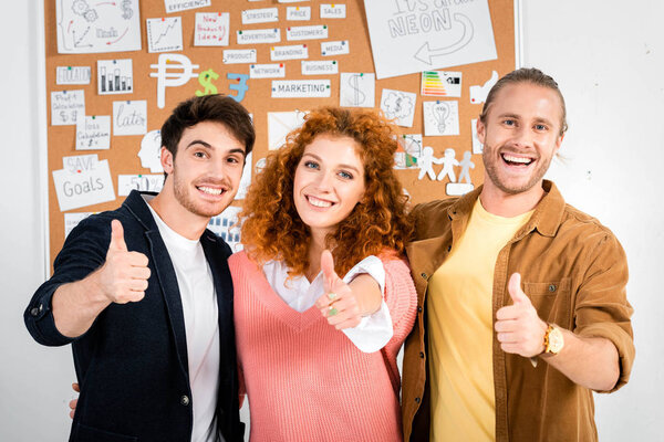 three smiling friends showing thumbs up and looking at camera 