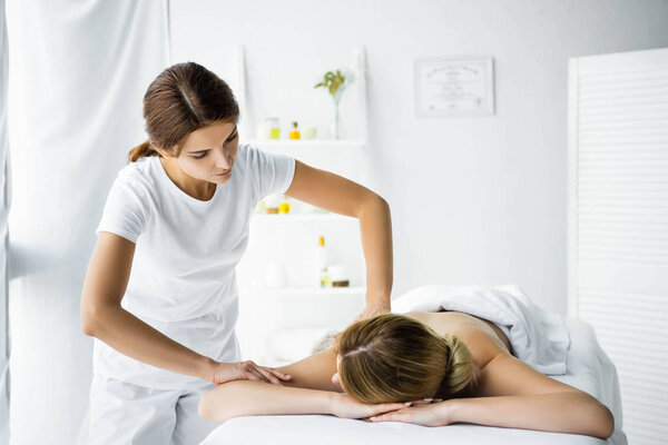 привлекательный массажист, делающий массаж спины женщине в спа
 