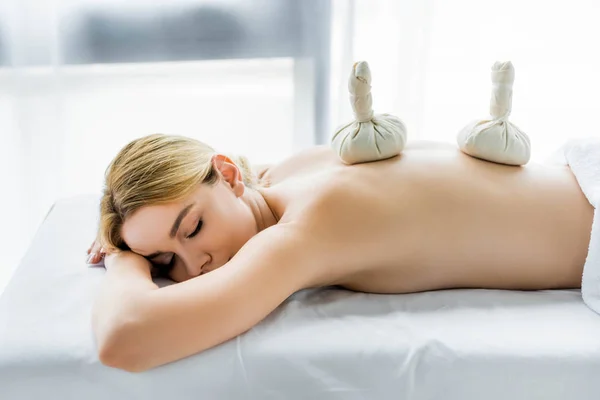 attractive woman lying on massage mat with herbal balls on back