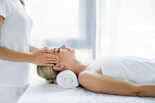 обрезанный вид массажера, делающего массаж лица привлекательной женщине
 