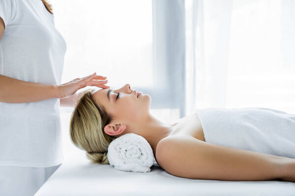 обрезанный вид массажера, делающего массаж лица привлекательной женщине
 