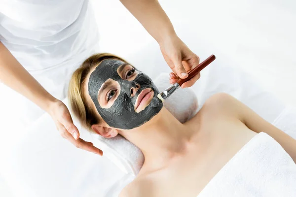 女性の顔に粘土マスクを適用する美容師のトリミングビュー — ストック写真