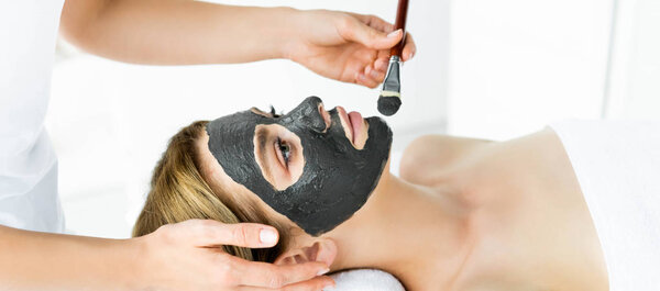 panoramic shot of beautician applying clay mask on face of woman 