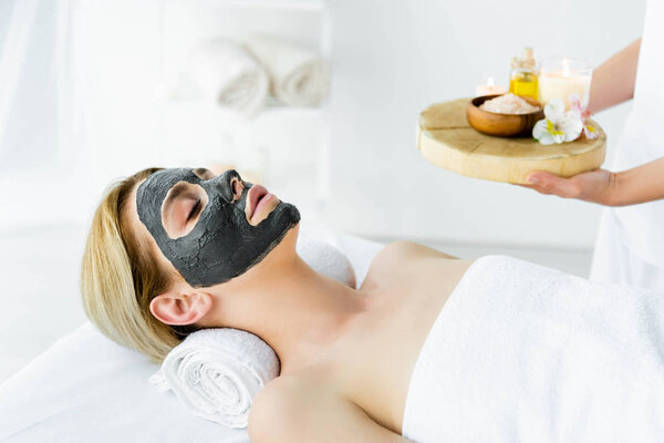 attractive woman with clay mask on face lying in spa 