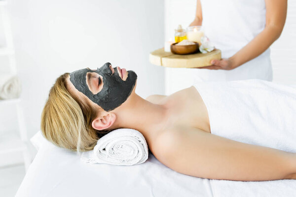 attractive woman with clay mask on face lying in spa 