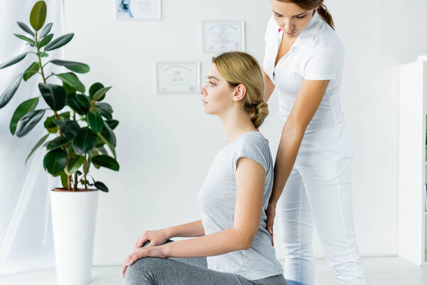 side view of attractive patient sitting and chiropractor touching her back 