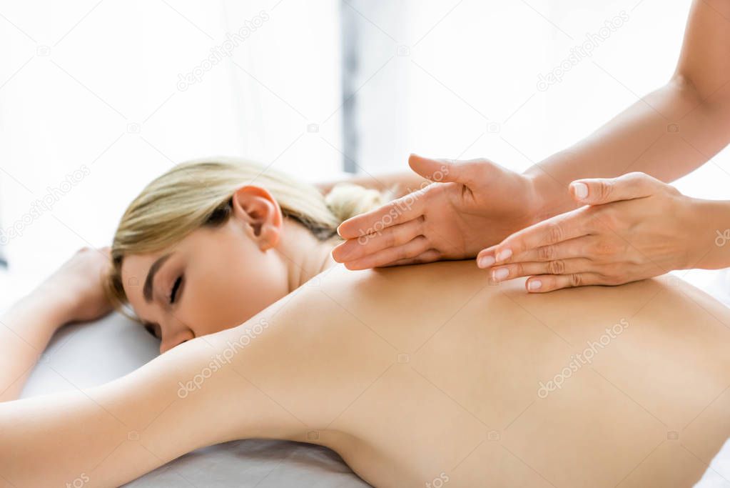 cropped view of masseur doing back massage to attractive woman in spa 